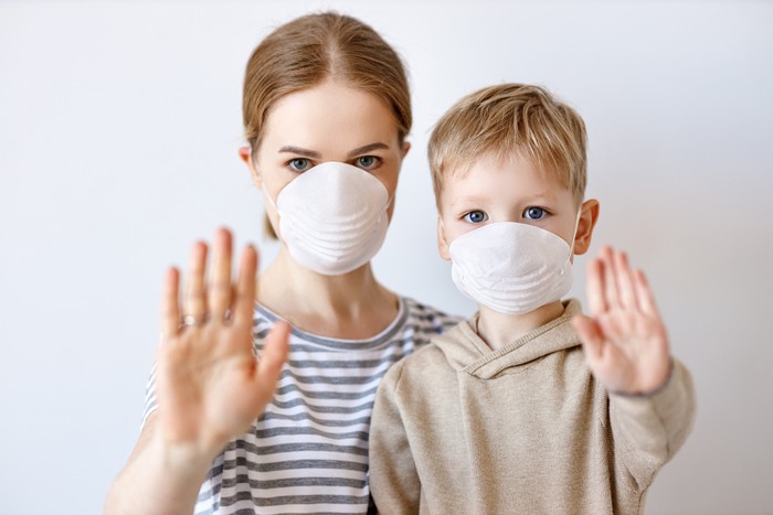 Adult woman and little boy in medical masks showing stop gesture and looking at camera during coronavirus epidemic against gray background