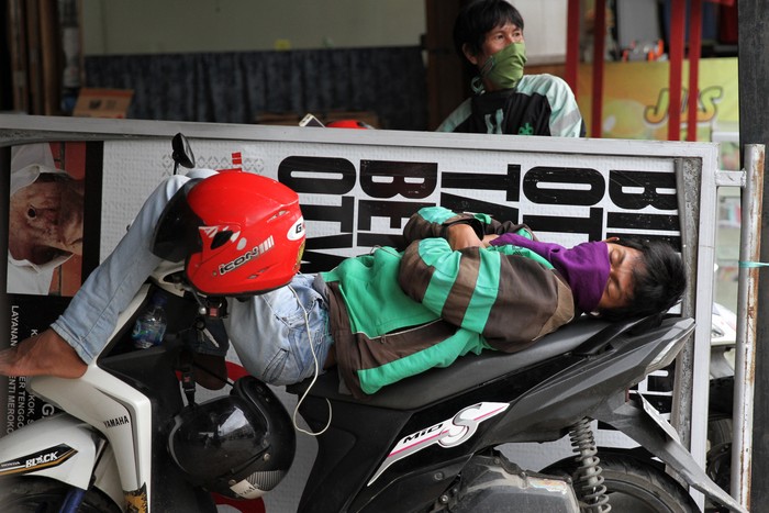 Sejak imbauan pemerintah untuk melakukan jaga jarak fisik terkait COVID-19, pendapatan para pengemudi ojek daring turun drastis. Kini penumpang kian sepi.