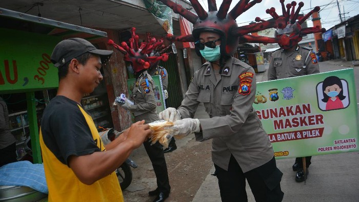 SOSIALISASI PENGGUNAAN MASKER DENGAN CARA UNIK Anggota polisi lalu lintas Polres Mojokerto melakukan pemeriksaan suhu tubuh pengendara motor saat sosialisasi penggunaan masker dengan memakai helm virus corona di pasar tradisional Sawahan, Kecamatan Bangsal, Kabupaten Mojokerto, Jawa Timur, Rabu (8/4/2020). Polres Mojokerto memakai cara unik untuk menyadarkan masyarakat terkait kewajiban menggunakan masker saat keluar rumah serta membagi masker gratis untuk mengantisipasi penyebaran COVID-19. ANTARA FOFO/Syaiful Arif/foc.