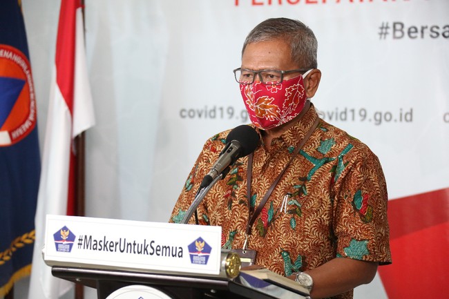 Tampak pria 58 tahun itu memakai masker berwarna oranye yang mirip di logo BNPB. Masker yang sama juga dipakai beberapa pria yang ikut mendampingi Achmad Yurianto di kesempatan tersebut. Hari-hari berikutnya, masker kain pilihan Achmad Yurianto seolah menjelma sebagai aksesori dengan fashion statement tersendiri.Masker yang dipakainya sesekali matching dengan baju batiknya. Pernah ia memakai masker bermotif batik nuansa floral dengan warna merah muda keunguan sebagai dasarnya. (Foto: dok. BNPB)
