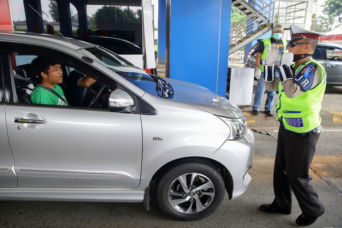 Petugas kepolisian melakukan pengecekan kepada kendaraan yang melintasi gerbang tol Pasar Rebo Utama. Ini bagian dari penerapan PSBB di Jakarta.