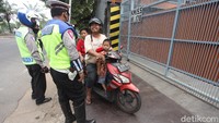 Petugas memeriksa seorang pengendara yang tak mengenakan masker saat melintas di area sekitar check point pengawasan PSBB di kawasan Jakarta Barat. Pengendara yang tidak mengenakan masker diarahkan untuk putar balik kembali ke arah Tangerang.