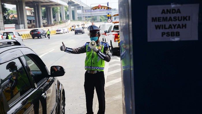 Petugas kepolisian melakukan pengecekan kepada kendaraan yang melintasi gerbang tol Pasar Rebo Utama. Ini bagian dari penerapan PSBB di Jakarta.