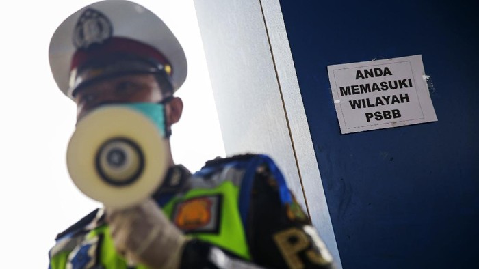 Petugas kepolisian melakukan pengecekan kepada kendaraan yang melintasi gerbang tol Pasar Rebo Utama. Ini bagian dari penerapan PSBB di Jakarta.
