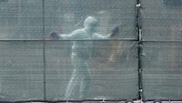 Seorang petuga berpakaian hazmat menutup pintu gerbang ke arah area parkir truk-truk es yang disiapkan untuk menyimpan jenazah korban corona (AFP/ANGELA WEISS)