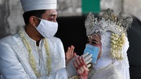 Calon pengantin Novi Herdjanto (kiri) merapikan masker pasangannya Mellawati Isnoer sebelum melangsungkan prosesi akad nikah di Kantor Urusan Agama Kecamatan Menteng, Jakarta Pusat, Sabtu (11/4/2020).
