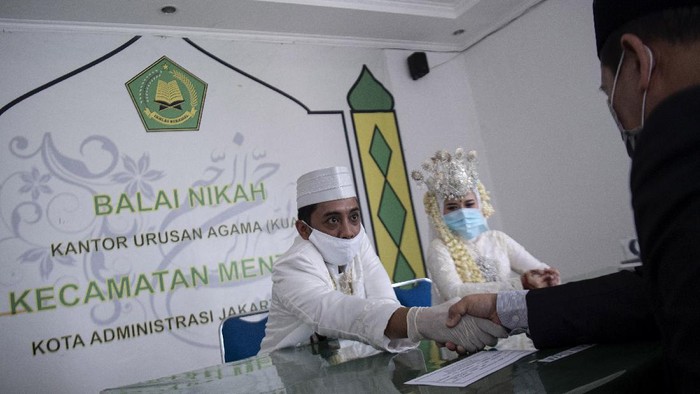 Penghulu memberikan buku nikah kepada pasangan pengantin, saat prosesi pernikahan, di Balai Nikah Kantor Urusan Agama (KUA) Padang Barat, Kota Padang, Sumatera Barat, Sabtu (11/4/2020). Penyelenggaraan pernikahan tetap dilaksanakan di kantor KUA setempat dengan mematuhi protokol pencegahan COVID-19 sesuai panduan dari Kementerian Agama, di antaranya tidak boleh lebih dari 10 orang dan harus menggunakan masker serta sarung tangan. ANTARA FOTO/Iggoy el Fitra/hp.