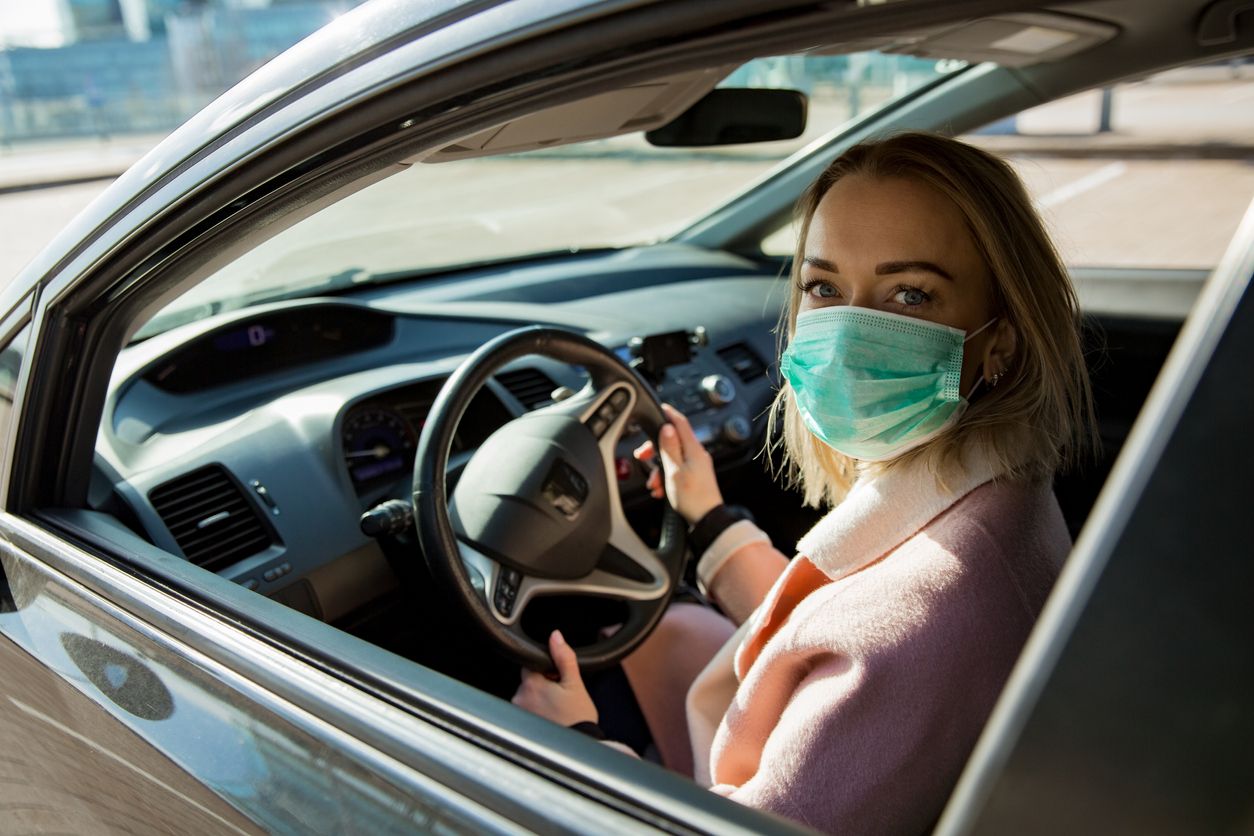 Woman in protective mask driving a car on road. Safe traveling.