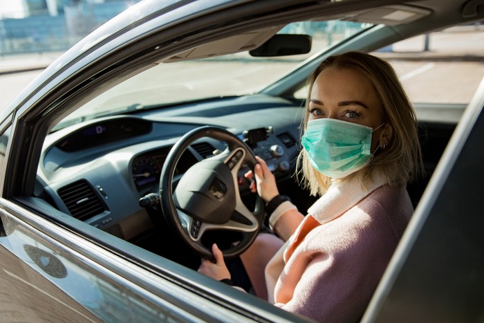 Naik mobil pakai masker Woman in protective mask driving a car on road. Safe traveling.