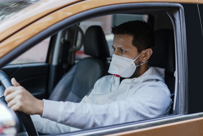 Woman in protective mask driving a car on road. Safe traveling.