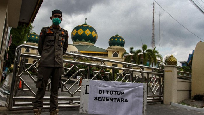 Petugas Satpol PP Kota Pekanbaru berjaga di depan pintu masuk Masjid Agung Ar-Rahman yang ditutup sementara, di Pekanbaru, Riau, Jumat (20/3/2020). Penyelenggaraan ibadah Salat Jumat ditiadakan sementara di Masjid ini guna mengantisipasi dan meminimalisir terjadinya penyebaran virus Corona (COVID-19). ANTARA FOTO/Rony Muharrman/pd.