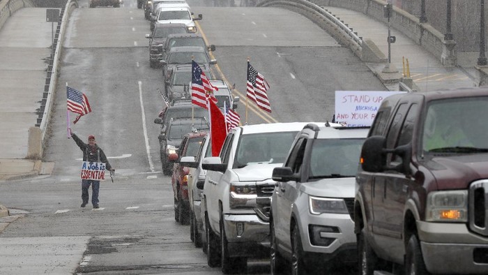 Chris Schornak walks past gridlocked protester in Lansing, Mich., Wednesday, April 15, 2020. Flag-waving, honking protesters drove past the Michigan Capitol on Wednesday to show their displeasure with Gov. Gretchen Whitmers orders to keep people at home and businesses locked during the new coronavirus COVID-19 outbreak. (AP Photo/Paul Sancya)