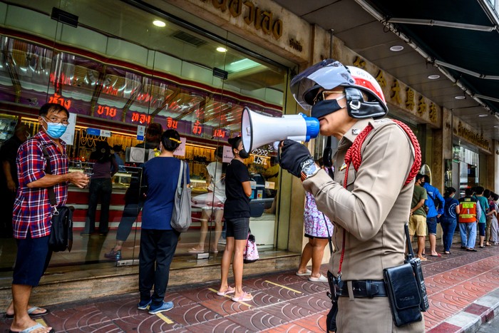 A police officer enforces social distancing as people wearing face masks amid fears of the spread of COVID-19 coronavirus line up to sell their jewelries in front of a gold shop in Bangkoks Chinatown on April 15, 2020. - Hundreds of Bangkok residents rushed to goldsmith shops in order to sell their jewelries as gold prices reached its highest levels since 2012. (Photo by Mladen ANTONOV / AFP)