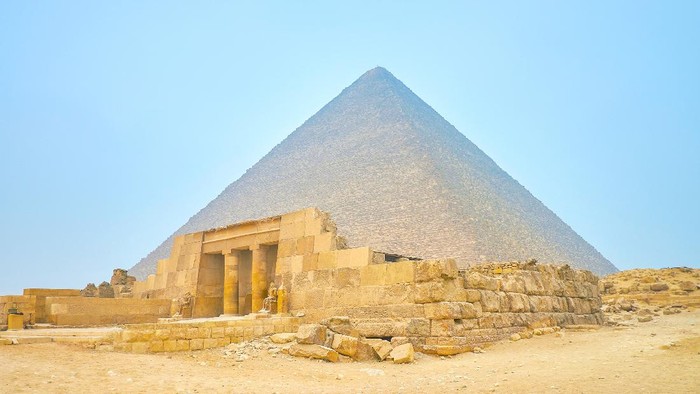 The preserved entrance with columns of the Mastaba (Tomb) of Queen Meresankh III with the Pyramid of Khufu on the background, Giza complex, Egypt