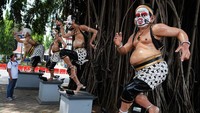 Warga tampak meilhat dan memotret Patung wayang yang dipasangi masker kain di halaman Balai Kota Solo, Jawa Tengah, Minggu (19/4/2020).