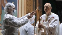 Seorang relawan memakai APD saat menyalakan lilin dari seorang pendeta saat Paskah di sebuah gereja di Bucharest, Rumania. AP Photo/Vadim Ghirda