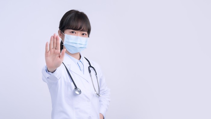 ilustrasi dokter memakai masker Young female doctor woman wearing mask, making stop sign gesture, saying No isolated on white background, refusing virus disease, close up, blank.