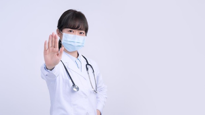 ilustrasi dokter memakai masker Young female doctor woman wearing mask, making stop sign gesture, saying No isolated on white background, refusing virus disease, close up, blank.
