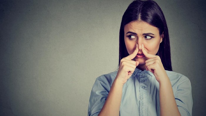 kentut bau tidak sedap Woman pinches nose with fingers looks with disgust away something stinks bad smell isolated on gray background.
