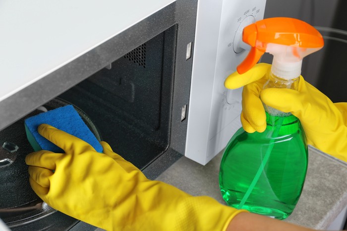 Close up of female hands with protective gloves scrubbing oven in kitchen