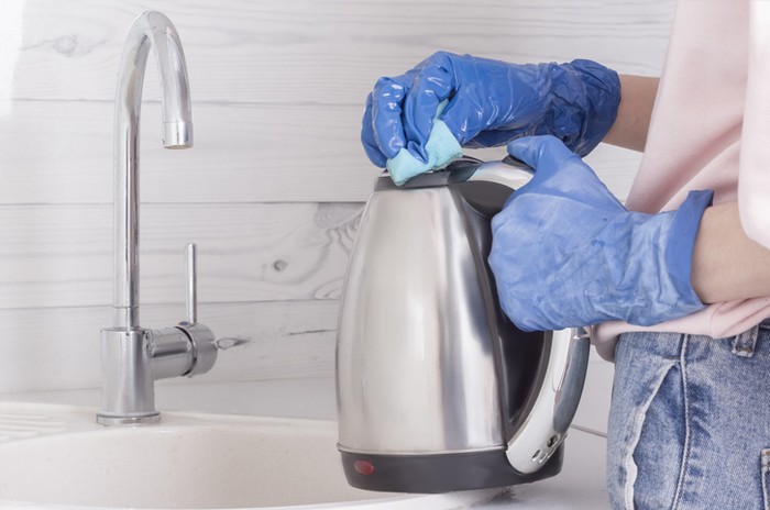 Close up of female hands with protective gloves scrubbing oven in kitchen