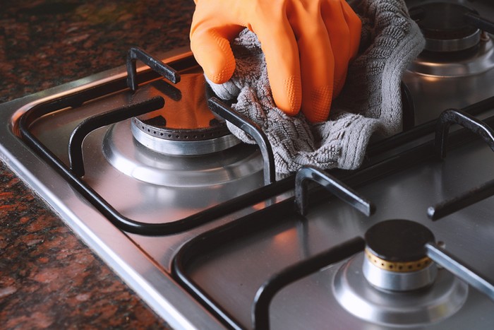 Close up of female hands with protective gloves scrubbing oven in kitchen