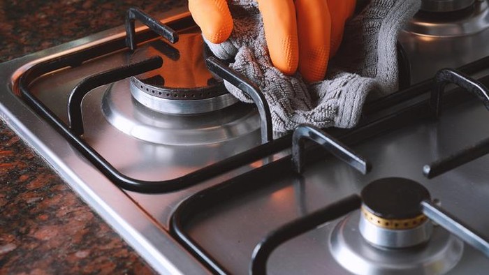 Close up of female hands with protective gloves scrubbing oven in kitchen