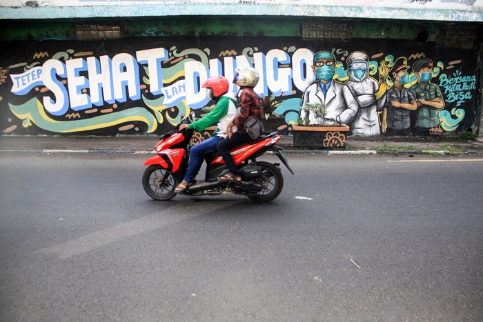 Pengendara melintas di depan mural tentang pandemi COVID-19 di Kawasan Bangil, Pasuruan, Sidoarjo, Jawa Timur, Senin (20/4/2020). Mural tersebut dibuat bertujuan untuk mensosialisasikan dan mengedukasi warga agar tetap waspada terhadap potensi penyebaran virus corona atau COVID-19. ANTARA FOTO/Umarul Faruq/wsj.