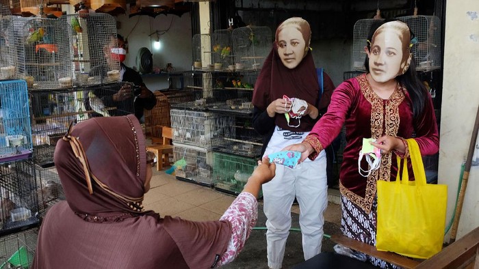 RAYAKAN HARI KARTINI Dua wanita memakai topeng bergambar pahlawan nasional, Raden Ajeng Kartini saat membagikan masker kain di Pasar Hewan Depok, Solo, Selasa (21/4/2020). Aksi untuk memperingati Hari Kartini tersebut juga diisi edukasi penggunaan masker kain kepada masyarakat, guna mendukung pemerintah mencegah penyebaran COVID-19. ANTARA FOTO/Maulana Surya/foc.