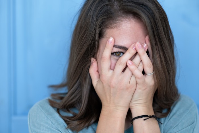 malu ekshibisionis takut Studio shot of brunette girl hiding eyes under hand while feeling ashamed. Caucasian young woman in white shirt covering face with hand. Human facial expressions and emotions