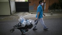 Seorang pria bermasker membawa troli untuk mengambil air di wilayah Caracas, Venezuela.