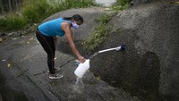 Seorang wanita yang menggunakan masker terlihat sedang mengisi air dengan menggunakan botol besar di sisi gunung wilayah Caracas. 