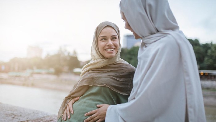 Cute and lovely pregnant Muslim woman and her Muslim friend, spending the time together on a city street.