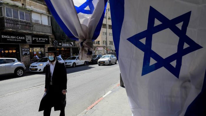 Seorang warga Yahudi memakai masker saat beraktivitas di luar rumah di tengah pandemi virus Corona An Ultra-Orthodox Jewish man, wearing a surgical mask due to the COVID-19 coronavirus pandemic, walks past Israeli flags set up in front of a shop ahead of Israels independence day due later in the week, in the centre of Jerusalem, on April 23, 2020. - Israel will celebrate its 72nd Independence Day on April 28-29 under novel coronavirus regulations, with official events and public celebrations cancelled. Israelis are required to wear faces masks when venturing outside in accordance to a governmental directive in order to combat the spread of COVID-19. (Photo by Emmanuel DUNAND / AFP)