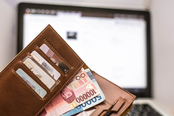 wallet with rupiah money inside in front of computer laptop monitor screen, online transaction concept
