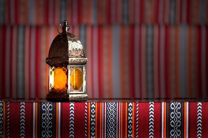 Couple of glowing Moroccan ornamental lanterns on the table. Greeting card, invitation for Muslim holy month Ramadan Kareem, festive blue night background with glittering golden bokeh lights.