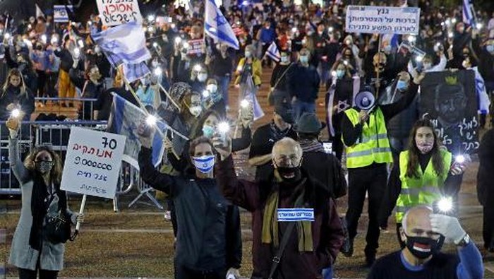 Israelis wearing protective masks lift placards as they take part in a demonstration on April 25, 2020, in Rabin Square in the coastal city of Tel Aviv, to protest what they consider threats to Israeli democracy, against the backdrop of negotiations between Prime Minister Benjamin Netanyahu and his ex-rival Benny Gantz. - The protesters stood two meters apart from each other, thereby respecting the social distancing measures in force to fight the COVID-19 pandemic. (Photo by JACK GUEZ / AFP)