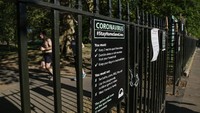 Sebuah papan informasi berisi imbauan agar warga mengurangi aktivitas di luar rumah untuk memutus rantai penyebaran virus Corona terlihat di kawasan Taman Battersea yang berada di kawasan London, Inggris. Hollie Adams/Getty Images.
