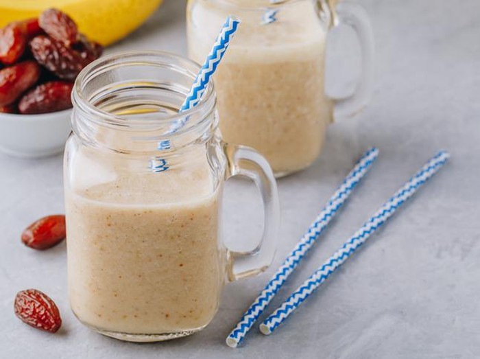Banana and chocolate smoothie in two jars, protein milkshake, nuts, chocolate cubes, dates, cinnamon sticks, healthy eating on a dark background.