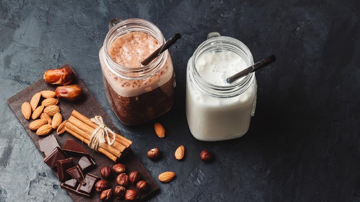 Banana and chocolate smoothie in two jars, protein milkshake, nuts, chocolate cubes, dates, cinnamon sticks, healthy eating on a dark background.