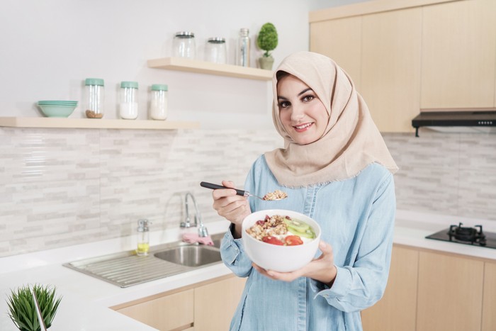 portrait of beautiful young woman wearing hijab with a bowl of granola with fresh fruit for breakfast