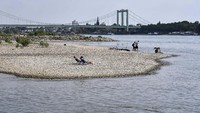 Orang-orang menikmati cuaca cerah di tepi sungai Rhine yang mengering.