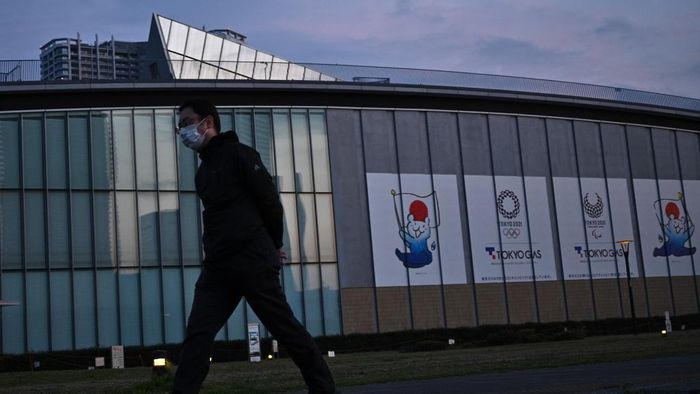 Olimpiade Tokyo A man wearing a face mask walks past logos of the Tokyo 2020 Olympics along a promenade in Tokyo in April 7, 2020. - Japans Prime Minister Shinzo Abe on April 7 declared a month-long state of emergency in Tokyo and six other parts of the country over a spike in coronavirus cases. (Photo by Philip FONG / AFP)
