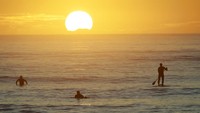 Warga berselancar sambil menikmati matahari terbit di Pantai Sumner di Christchurch, Selandia Baru.