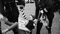 Aksi protes menuntut dihentikannya Perang Vietnam juga digelar di kawasan London pada tahun 1966. Seorang wanita yang membawa poster anti-perang diamankan sejumlah petugas saat ikut serta dalam aksi unjuk rasa menolak perang di kawasan Grosvenor Square, London, Inggris. Clive Limpkin/Express/Getty Images.