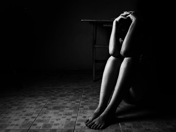 a woman sitting on ground with arm around lower head, sexual violence , sexual abuse, human trafficking concept with shadow edge in white tone