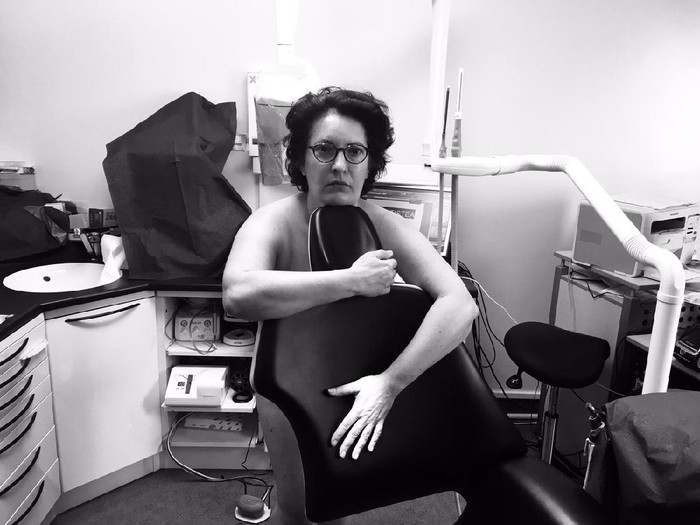 810206880 Dentist wearing eyeglasses gloves and mask examining a patient teeth with a dental probe and a mirror in a clinic box with equipment in the background