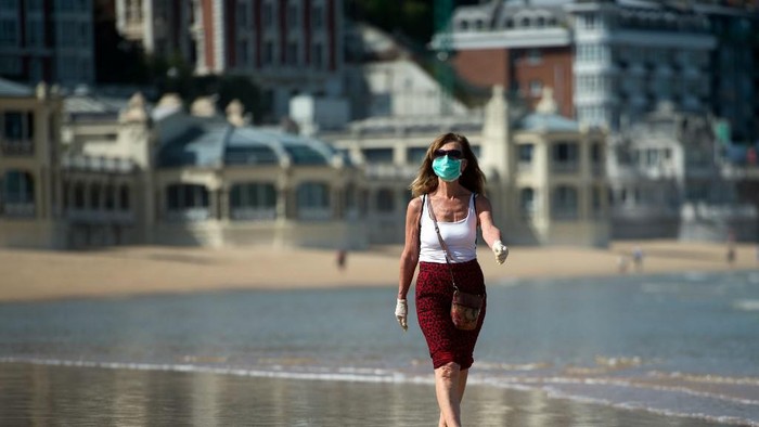 A woman wearing a face mask strolls on La Concha beach in San Sebastian, on May 2, 2020, during the hours allowed by the government to exercise, for the first time since the beginning of a national lockdown to prevent the spread of the COVID-19 disease. - All Spaniards are again allowed to leave their homes since today to walk or play sports after 48 days of very strict confinement to curb the coronavirus pandemic. After allowing children under 14 to go out since April 26, the government has again eased the conditions of the confinement imposed on March 14, which was one of the strictest in the world. (Photo by ANDER GILLENEA / AFP)