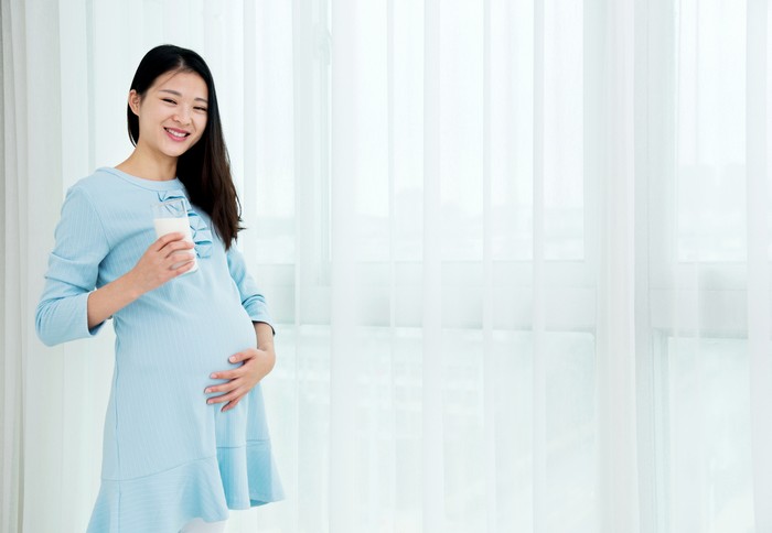 Pregnant woman drinking glass of milk copy space. Young expectant lady enjoying healthy drink. Healthcare, nutrition, vitamins, pregnancy concept