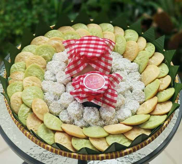 Javanese coconut milk and pandanus pancakes, served with sauce of coconut milk and palm sugar. Both the pancakes and the sauce are plated on traditional earthenware crockery set. Two wooden spoon are placed next to the plate. A folded woven straw mat lines the plate and cup. The meal is arranged on rustic wooden table that has a matching color with the earthenware. The image was taken outdoor using natural light.
